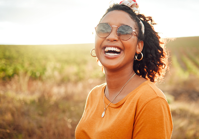 Woman in orange shirt standing in field and smiling