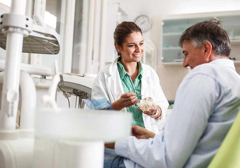 Dentist talking to patient while holding dental implant model