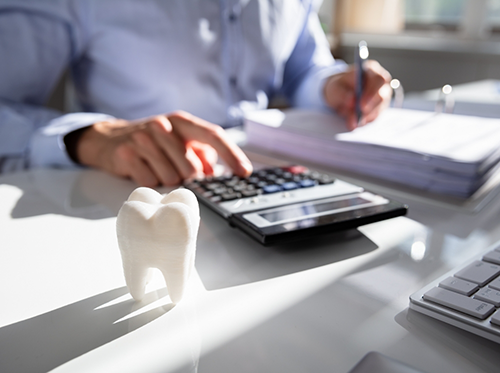 Person using calculator next to model of tooth