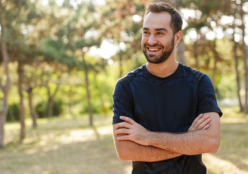 Man smiling outside with arms folded