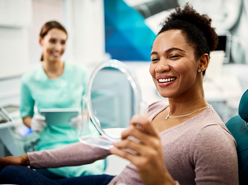 Woman in dental chair checking smile with handheld mirror